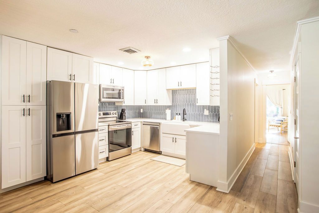 A modern kitchen with white cabinetry, stainless steel appliances, and a wooden floor.