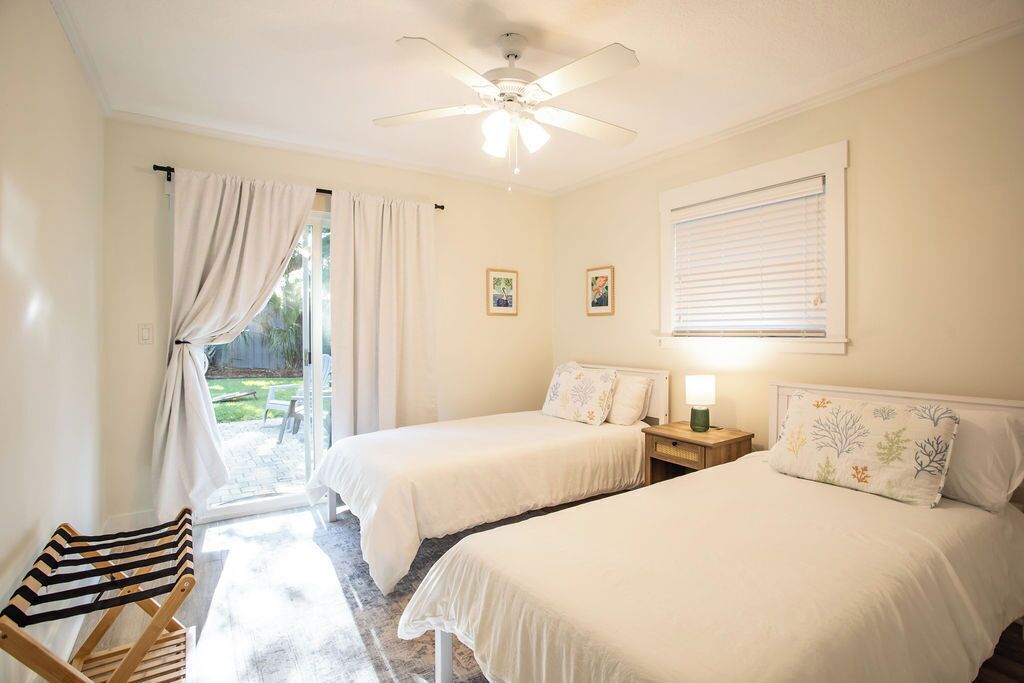 Un dormitorio con dos camas, un ventilador de techo, una ventana con persianas y vistas al exterior.