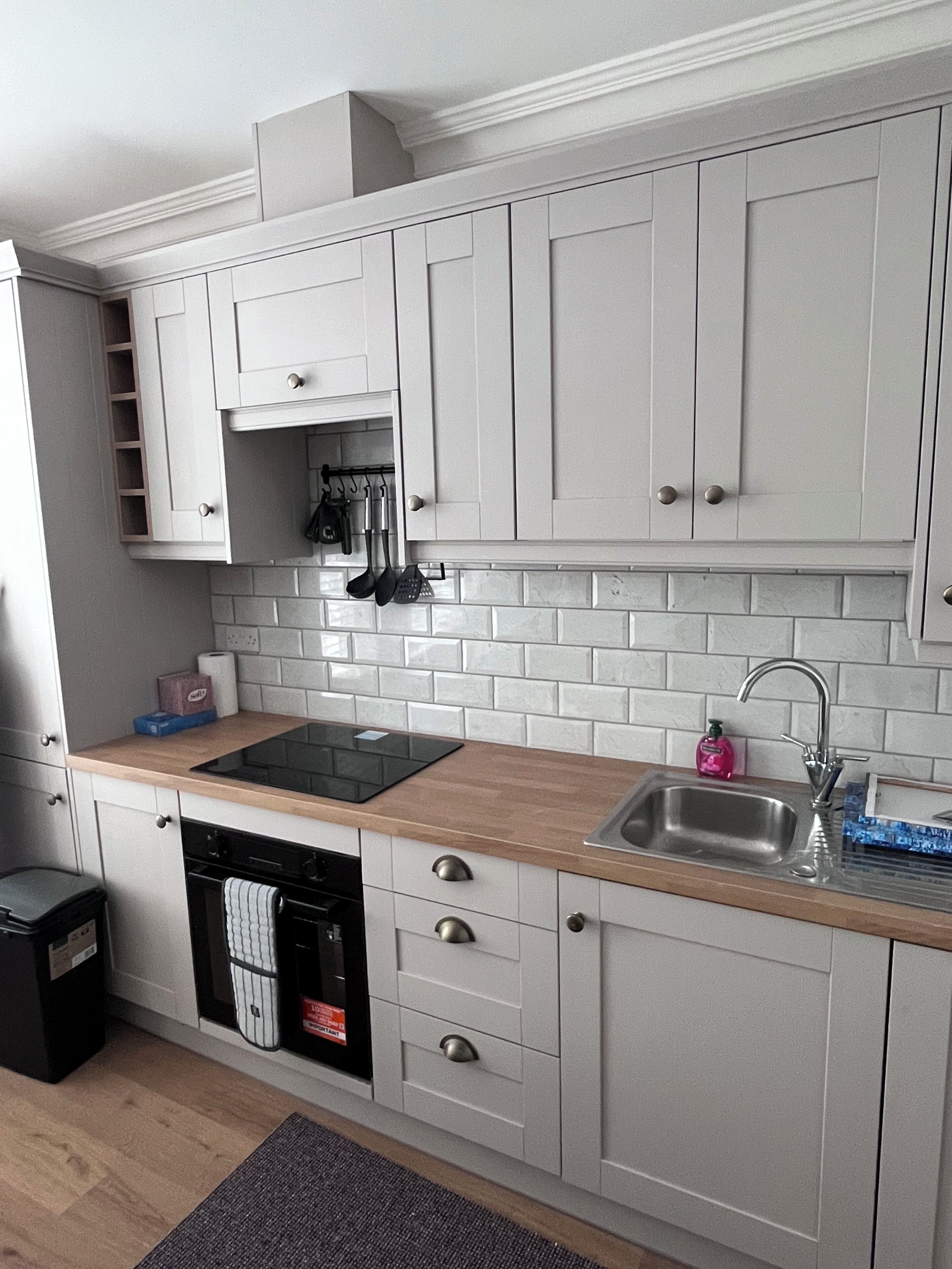 A modern kitchen with white cabinets, a wooden countertop, a built-in dishwasher, and a stainless steel sink.