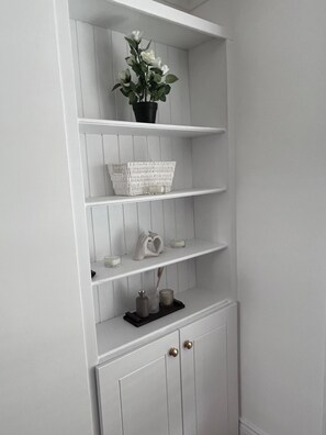 A white wooden shelving unit with a potted plant, a woven basket, and candle holders.