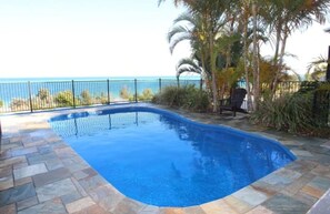 A swimming pool with a curved edge, surrounded by stone tiles and a metal fence. - 8 Coign Tangalooma Moreton island (moreton island)
