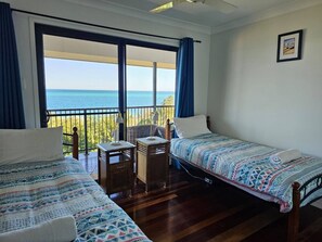 Habitación con dos camas, una mesita y una silla, y vista al mar a través de amplias ventanas.