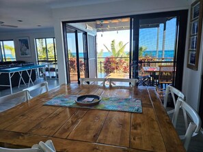 A dining area with a wooden table, chairs, and a view of the ocean through large glass doors. - 8 Coign Tangalooma Moreton island (moreton island)