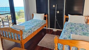 Ein Zimmer mit zwei Holzbett, einer Schiebetür, einem kleinen Tisch und Blick aufs Meer.