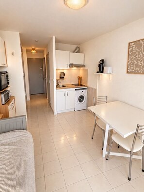 A compact kitchen with white cabinets, a microwave, a washing machine, and a dining area with a white table and chairs.