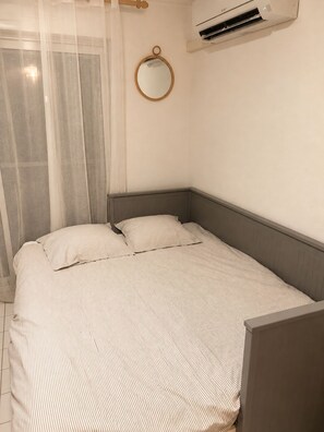 A bedroom with a bed, a round mirror, and an air conditioning unit.