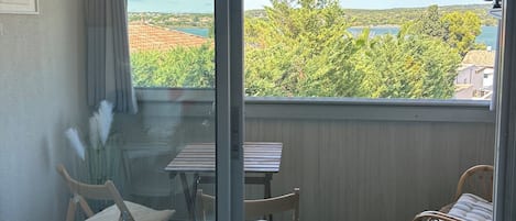 Un balcón con mesa y sillas, vistas a zonas verdes y edificios, y un cielo despejado.
