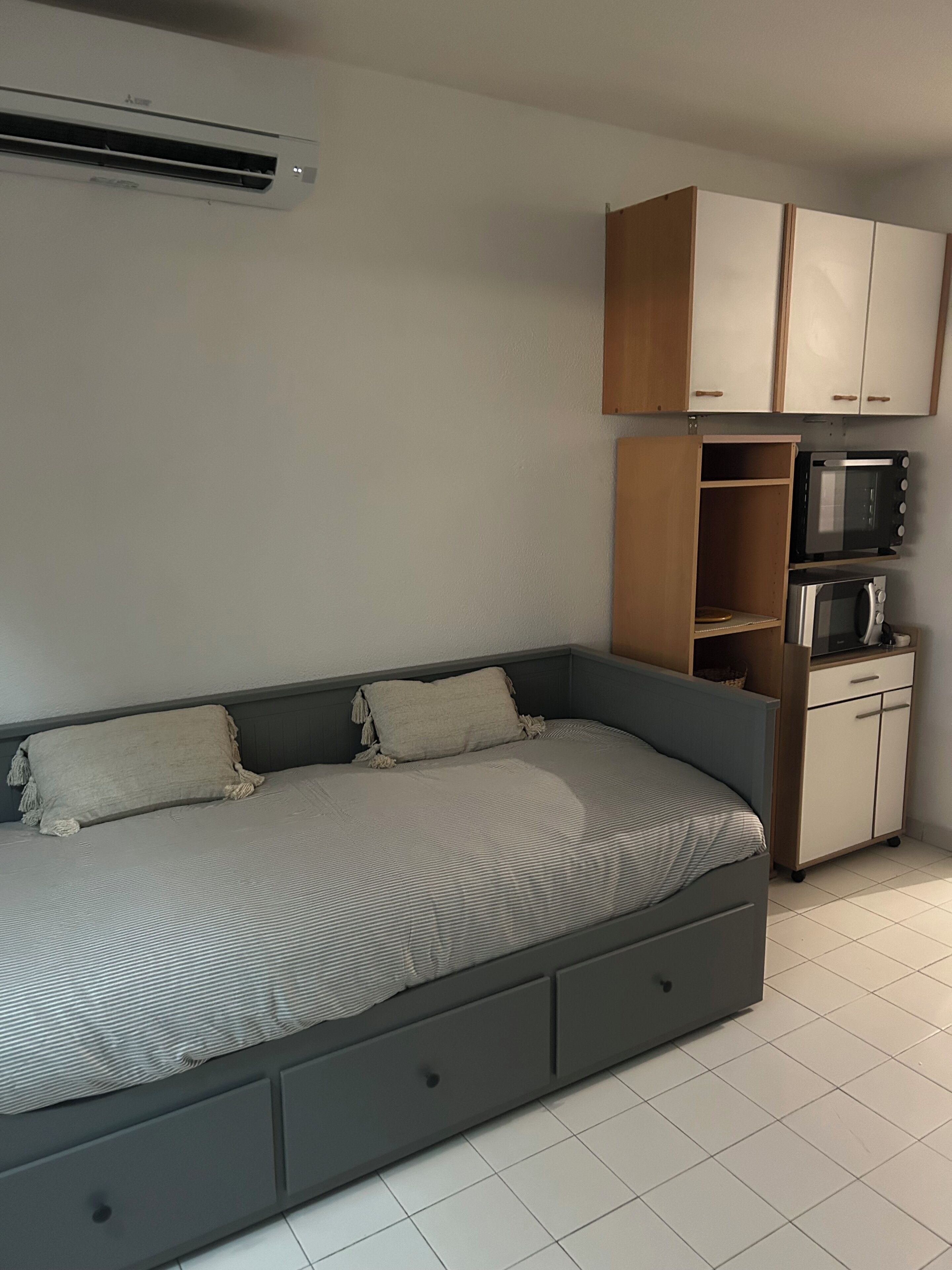 Een kamer met een bed, een magnetron en een kleine kitchenette.