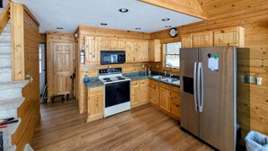 A wooden cabin-style kitchen with a stove, microwave, refrigerator, and wooden cabinets. - Eagle's Nest On The Water (Butternut)