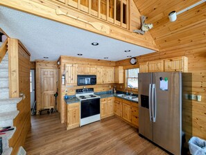 A wooden cabin-style kitchen with a stove, microwave, refrigerator, and wooden cabinets. - Eagle's Nest On The Water (Butternut)