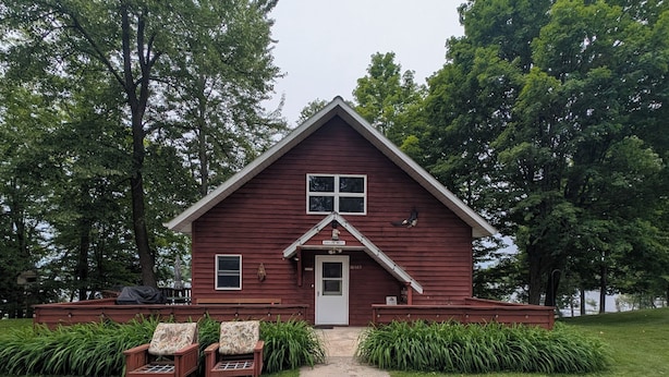 A red wooden cabin with a front porch, two chairs, and a pathway leading to the door. - Eagle's Nest On The Water (Butternut)