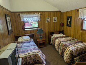 Ein Zimmer mit Holzvertäfelung, zwei Betten mit gemusterten Bettbezügen, einem Schreibtisch mit Lampe und gerahmten Bildern an der Wand.