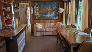 Et hyggeligt rum med en træsofa, et spisebord og et billede af en snefyldt skov på væggen.