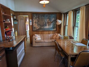 Ein gemütliches Zimmer mit einer Holzcouch, einem Esstisch und einem Bild von einem verschneiten Wald an der Wand.