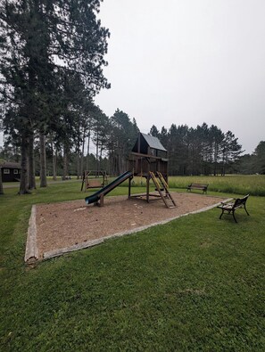 Ein Spielplatz mit Rutsche und Klettergerüst, umgeben von Gras und Bäumen.