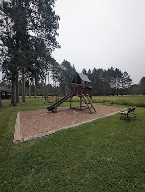 A playground with a slide and a climbing structure, surrounded by grass and trees. - Honeymoon On The Water with private dock & Beach (Butternut)