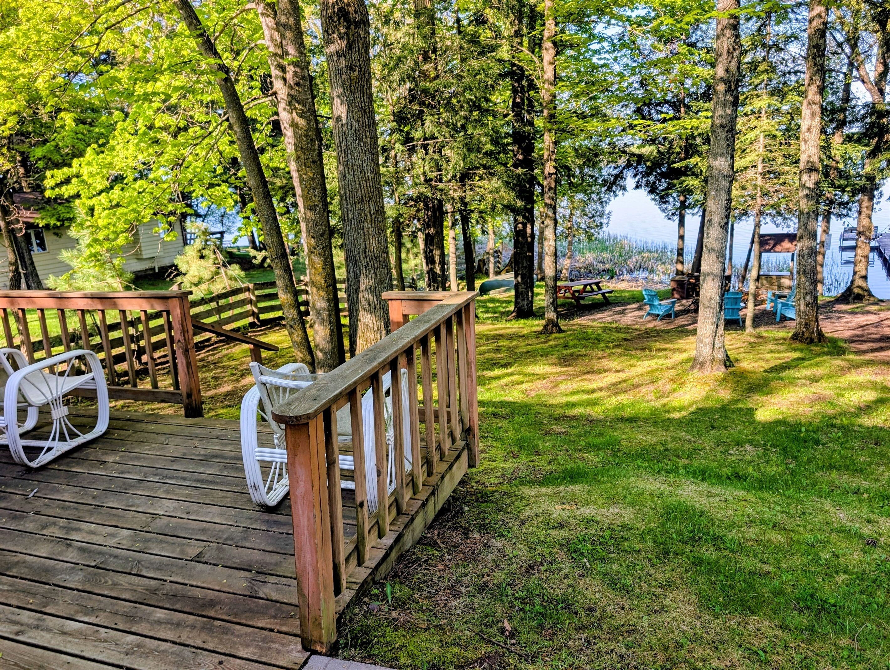 A wooden deck with a railing, white chairs, and a picnic table.