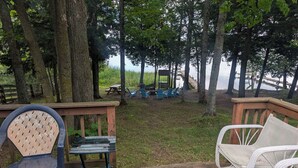Una terrassa de fusta amb mobles d'exterior, taula de picnic i cadires, amb vista a una massa d'aigua i arbres al fons.