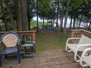 A wooden deck with outdoor furniture, a picnic table, and chairs, overlooking a body of water with trees in the background. - Honeymoon On The Water with private dock & Beach (Butternut)