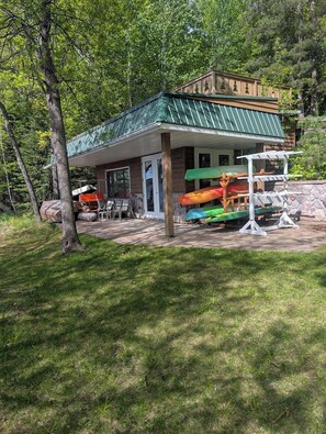 Eine Lodge mit einem grünen Dach, einem überdachten Sitzbereich im Freien und Kajaks, die unter einem Schutzdach gelagert werden.