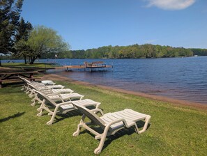Eine Uferlandschaft mit einer Reihe weißer Liegestühle und einem Holzsteg, der sich ins Wasser erstreckt.