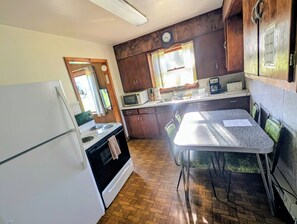Ett kompakt kök med kylskåp, spis, mikrovågsugn och ett matbord med stolar.