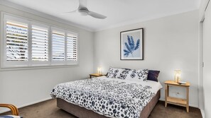 Una camera da letto con un letto, due comodini, una ventola a soffitto e una finestra con persiane.