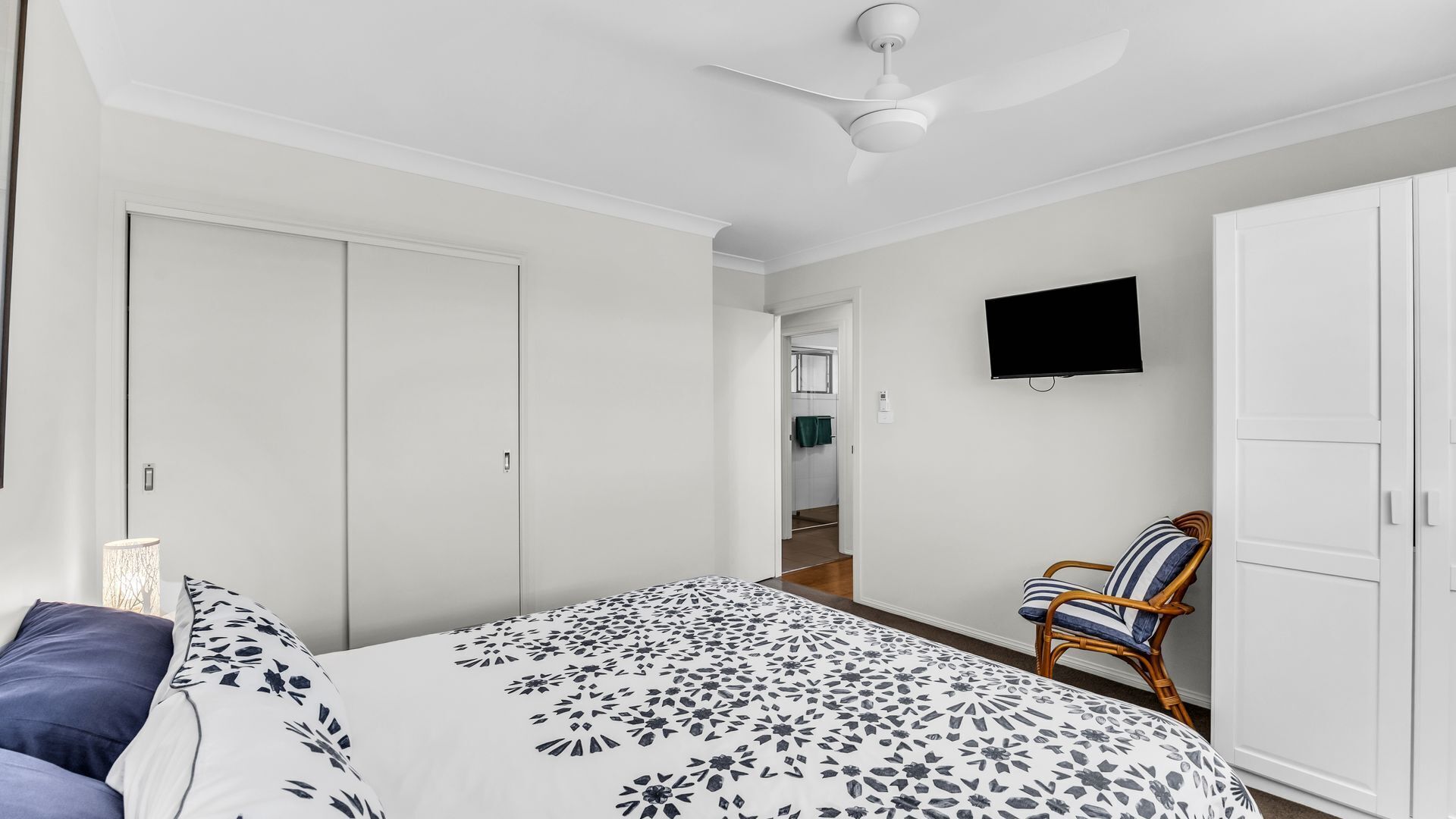 A bedroom with a bed, a chair, a wardrobe, a television, and a ceiling fan.