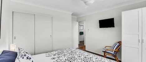 Un dormitorio con cama, una silla, armario, televisor y ventilador de techo.
