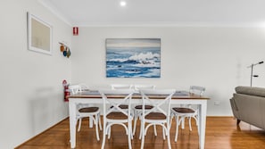 Un'area pranzo con un tavolo e sedie bianche, un dipinto che raffigura onde oceaniche e un estintore a parete.