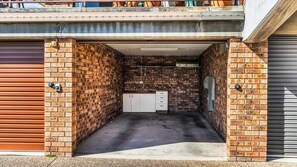 A garage with brick walls, a concrete floor, and a white storage unit. - Bermagui Beach Apartment - Corunna Street 1 U2 (Bermagui)
