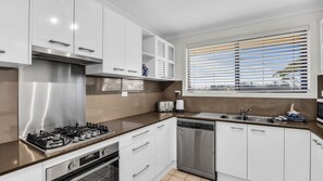 Una cucina moderna con mobili bianchi, elettrodomestici in acciaio inossidabile, lavastoviglie integrata e una finestra con persiane.