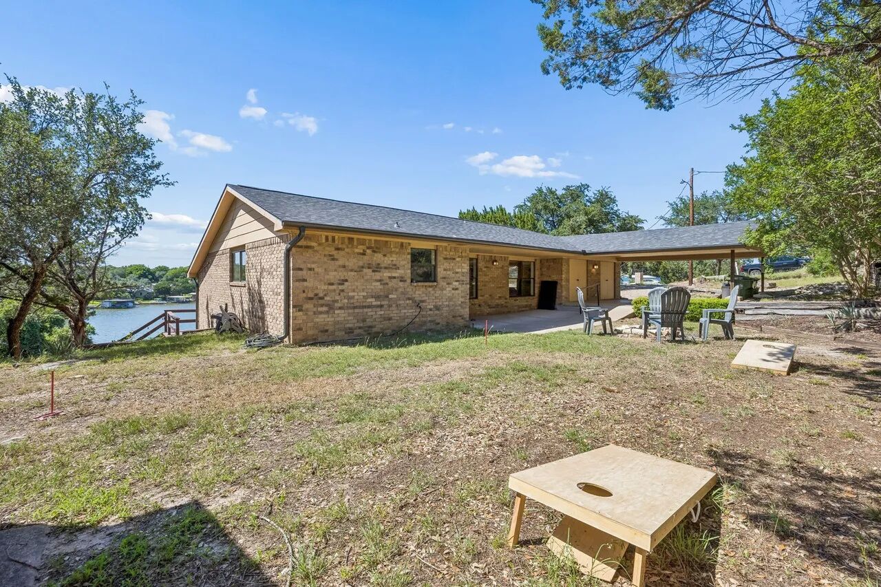 A stone building with a covered patio area, a wooden table, and a view of a body of water.