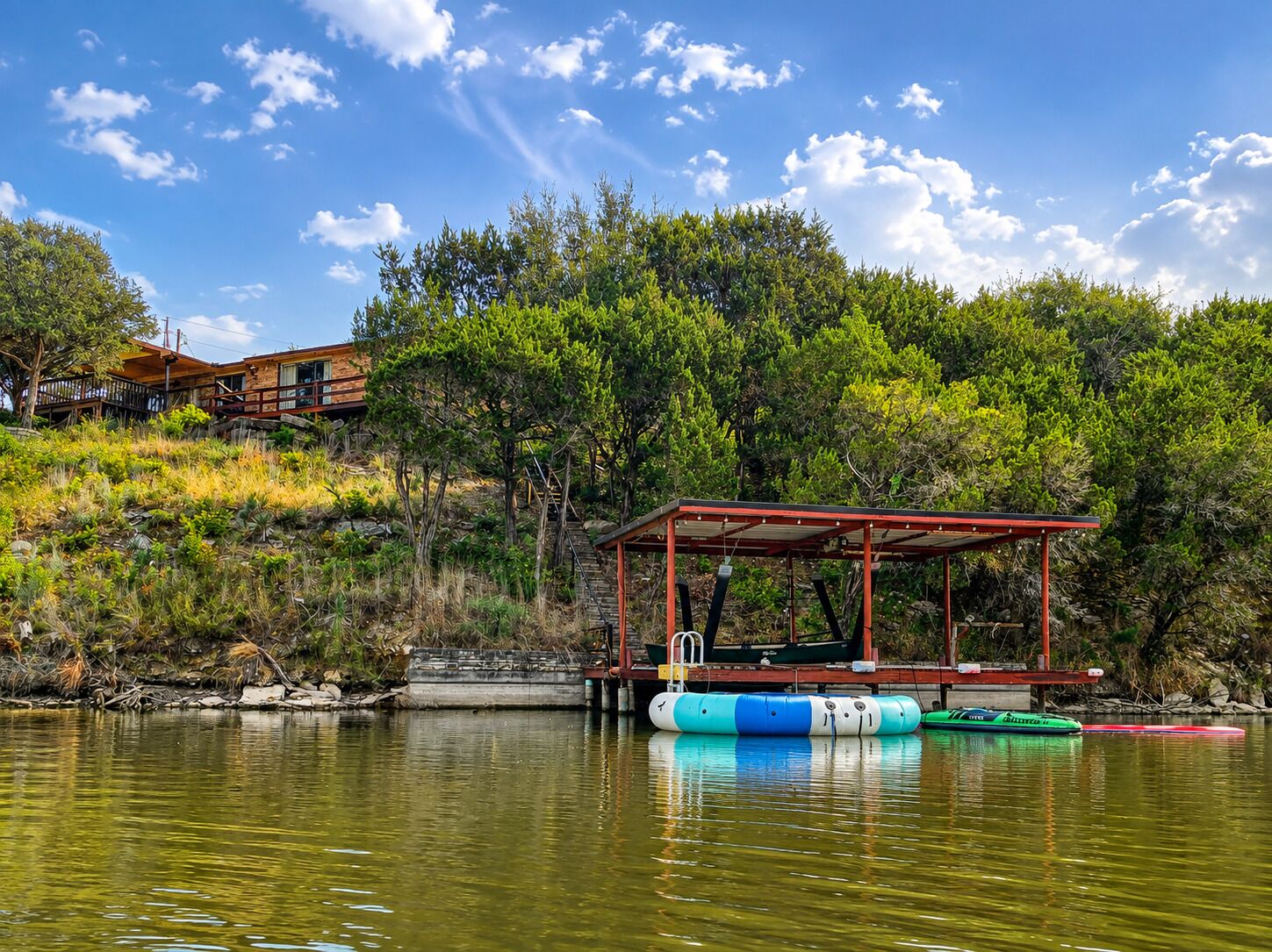 Private lakefront dock stocked for fun on the water, with life jackets, an inflatable trampoline, lily pad, inflatable kayak, canoe, and assorted inflatable tubes.