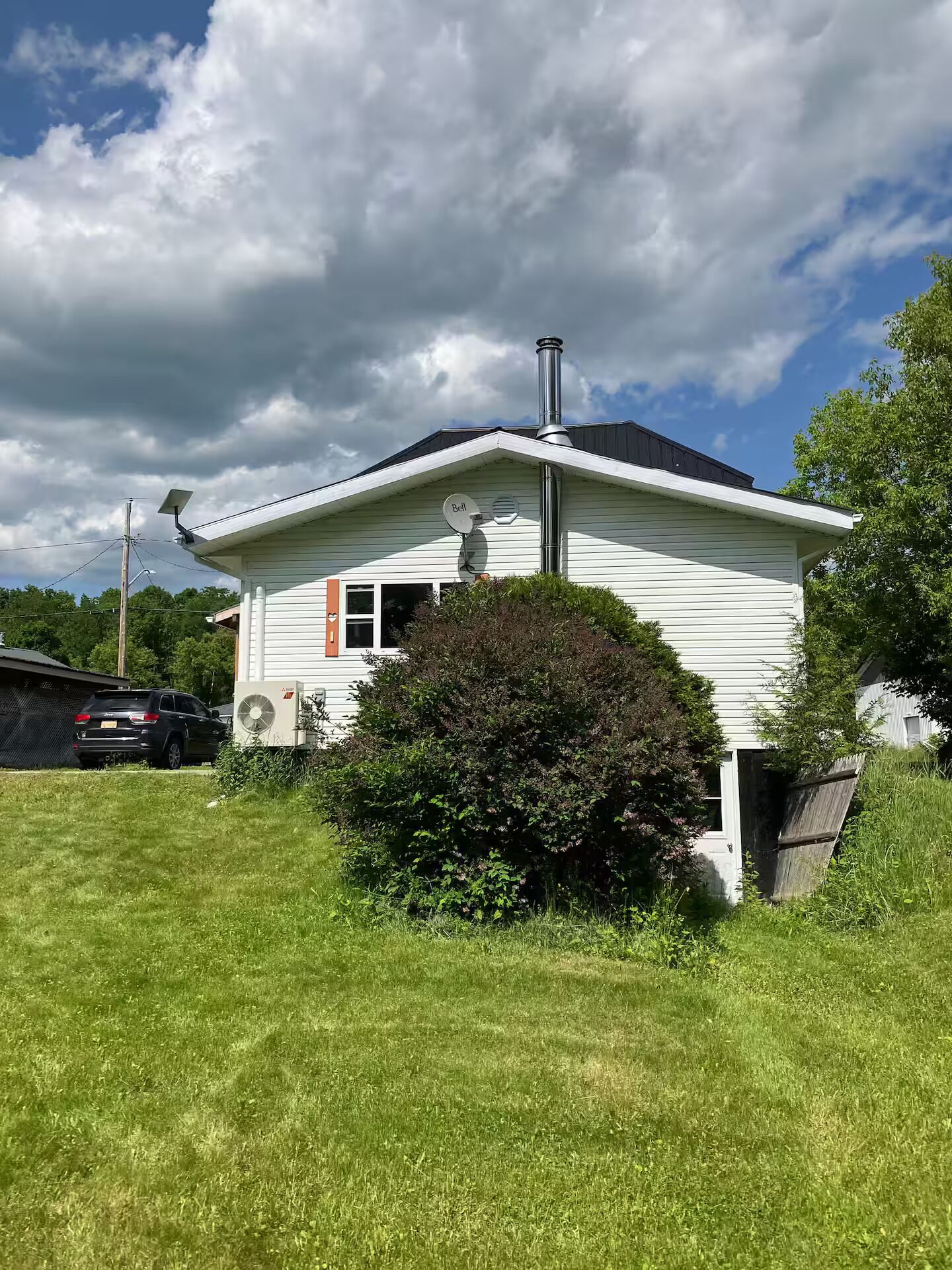 Une maison de plain-pied avec une cheminée, une antenne parabolique et un petit arbuste devant.