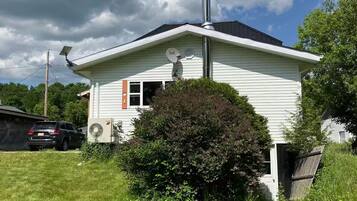 Une maison de plain-pied avec une cheminée, une antenne parabolique et un petit arbuste devant.
