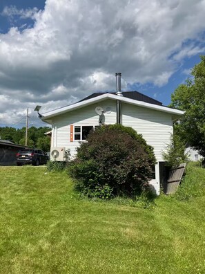 A single-story house with a chimney, satellite dish, and a small bush in front.
