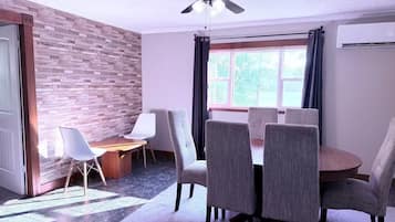 A dining area with a round table, four chairs, a ceiling fan, and a window with curtains.