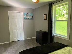 A room with a door, a window with a view of greenery, a bed, and a piece of wall art. - Riverfront Retreat Near Trans-Ca Hwy 2 | Sleeps 8 (Upper Kent)