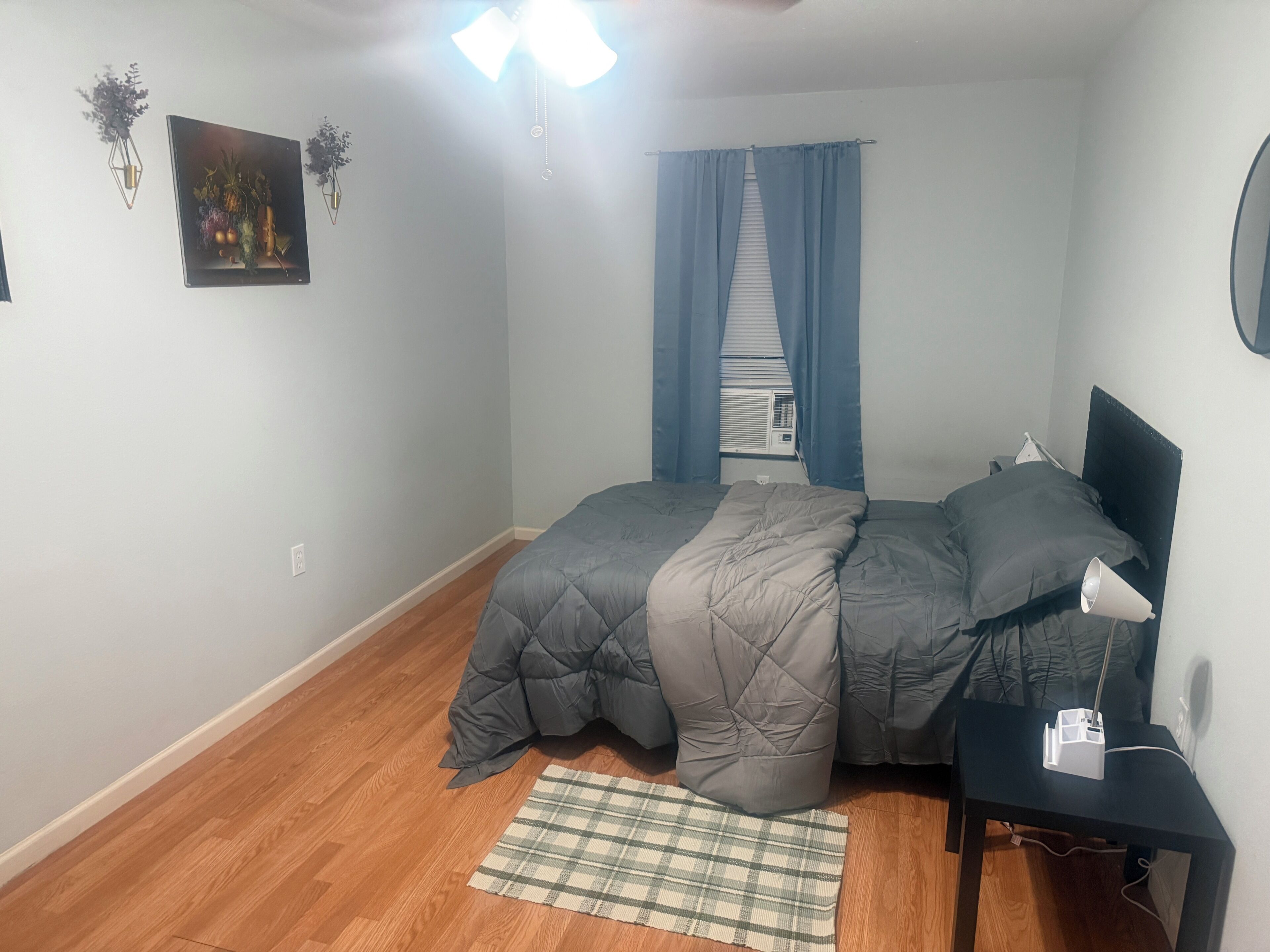 Une chambre à coucher comprenant un lit, une table de chevet, une lampe, une fenêtre avec des rideaux et un climatiseur fixé au mur.
