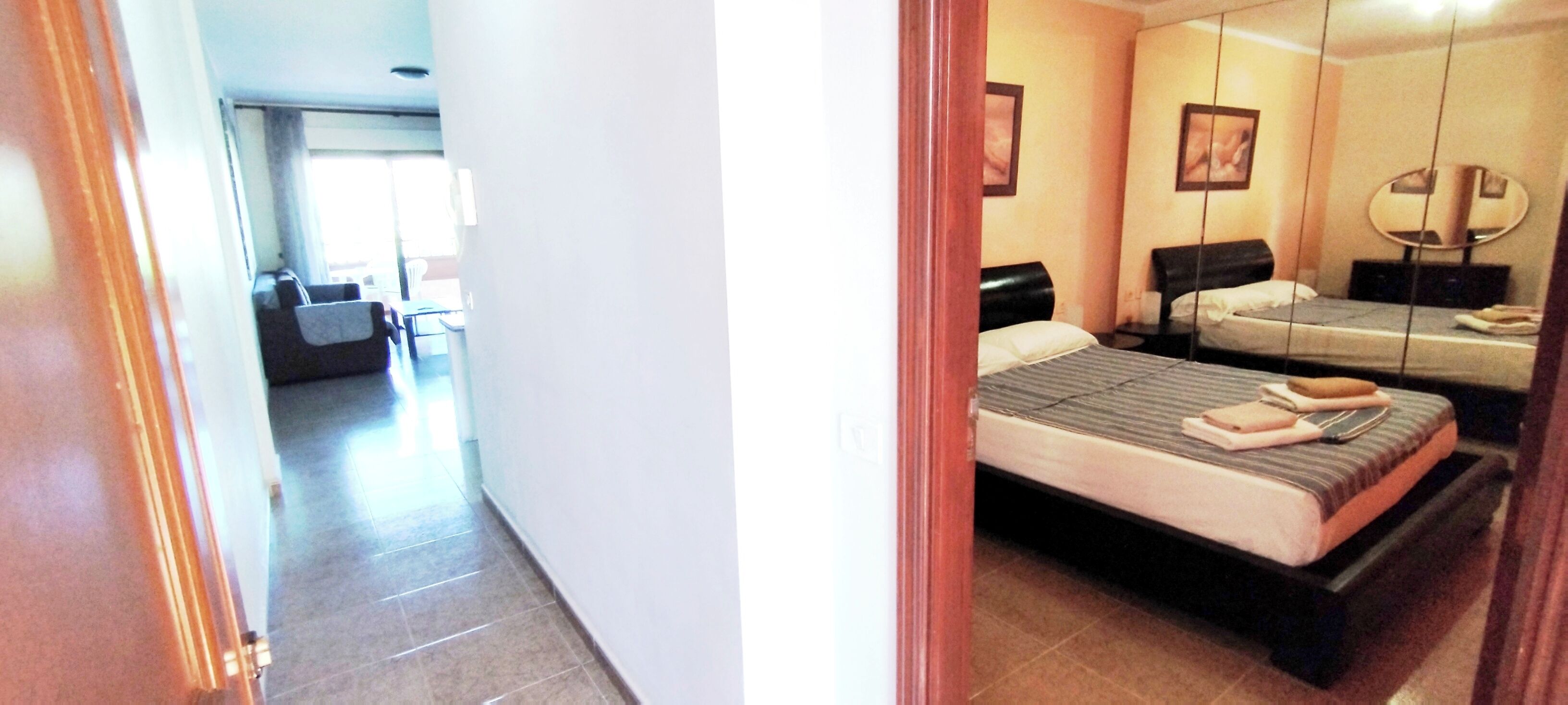 A hotel room with a bed, bedside table, and a mirror.