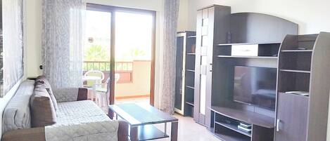 A living room with a sofa, a coffee table, a TV, and a sliding glass door leading to an outdoor area.