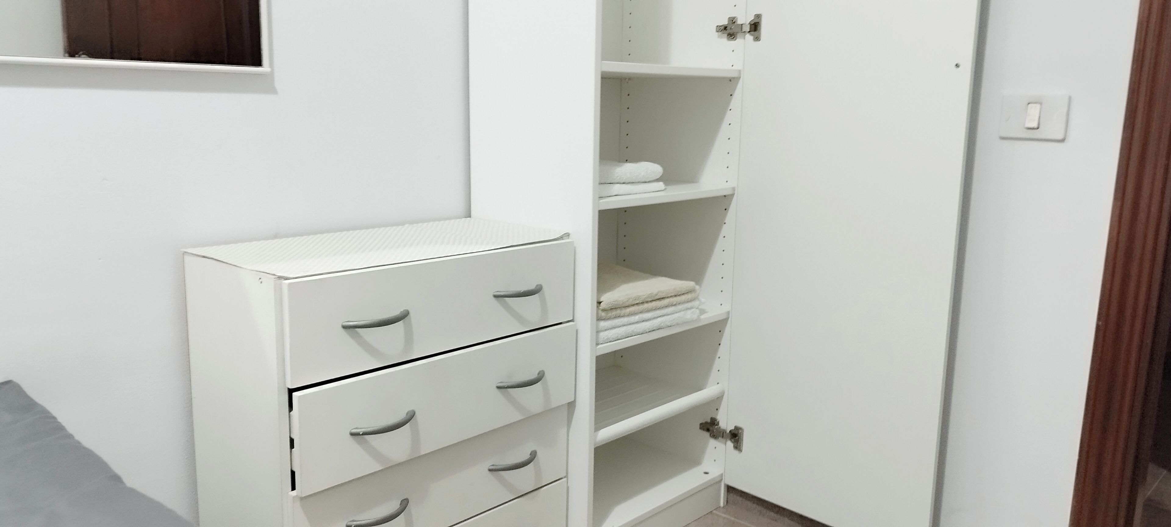 A white wardrobe with multiple drawers and shelves, a small mirror, and a door with a handle.
