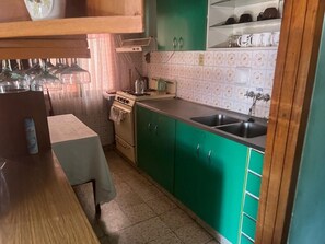 Een keuken met groene kastjes, een fornuis, een gootsteen en een tafel met een handdoek.