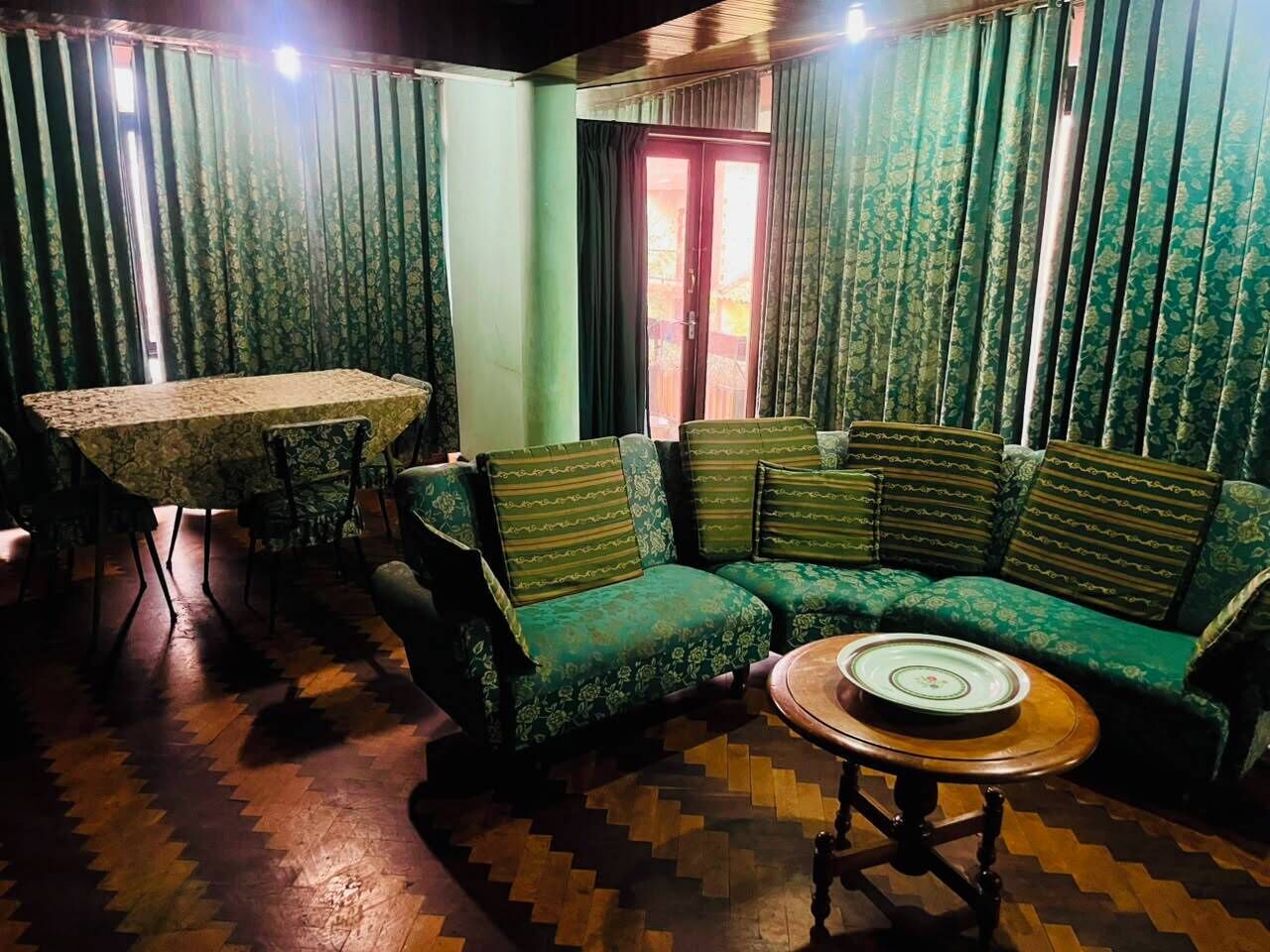 A room with a green patterned sofa, a round wooden table, and a dining table with chairs.