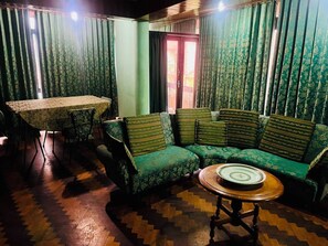 Een kamer met een groene gestreepte bank, een ronde houten tafel en een eettafel met stoelen.