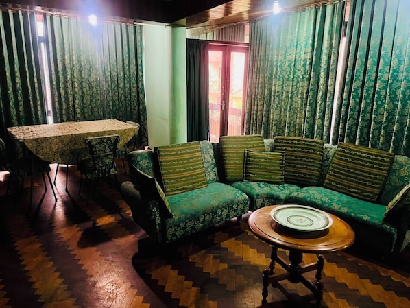 A room with a green patterned sofa, a round wooden table, and a dining table with chairs.