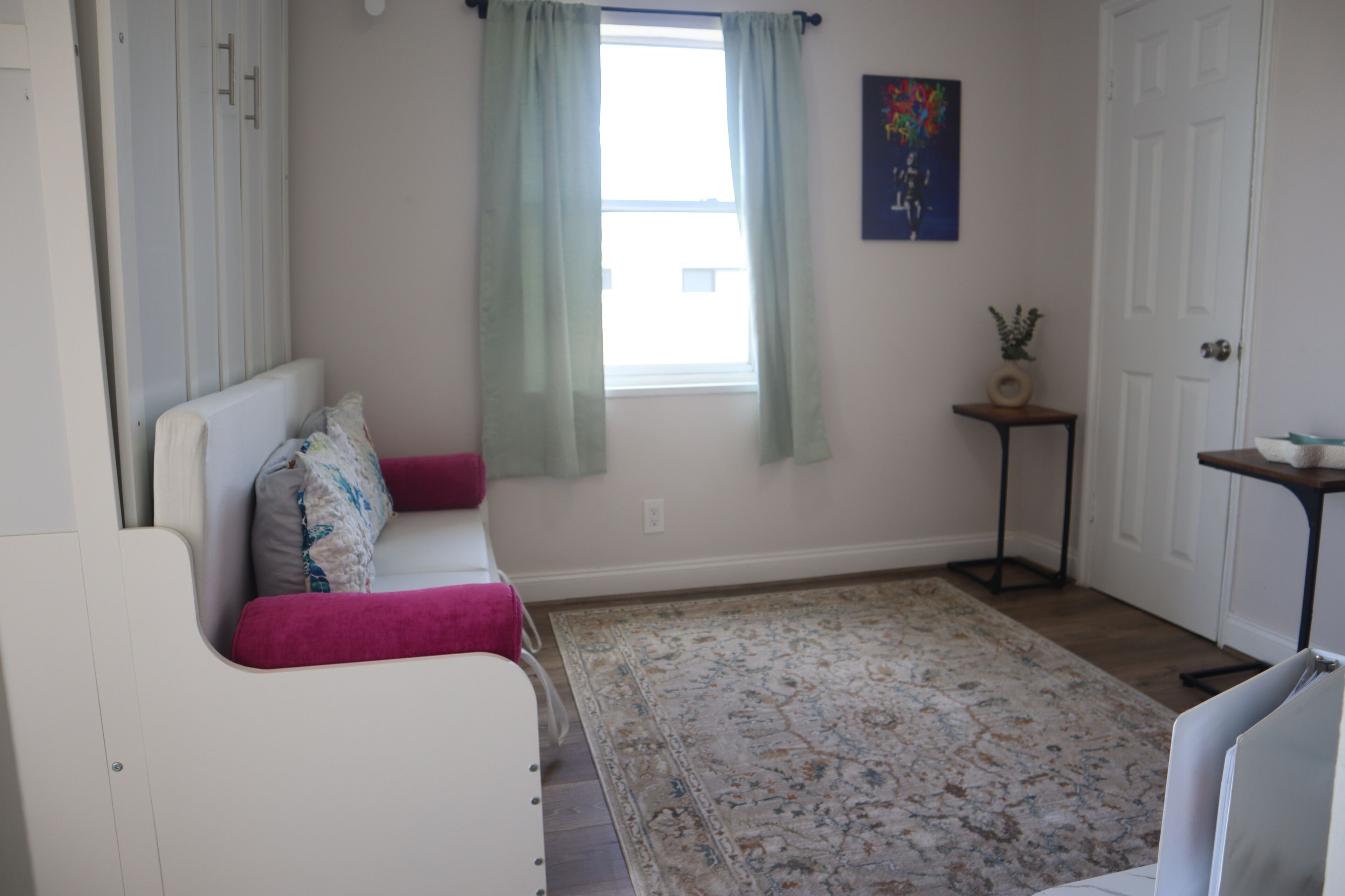 A room with a white sofa, a patterned rug, a small table, and a door.