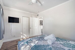 A bedroom with a bed, a ceiling fan, a TV mounted on the wall, and a door. - Lauderdale Breeze Villas (Fort Lauderdale)