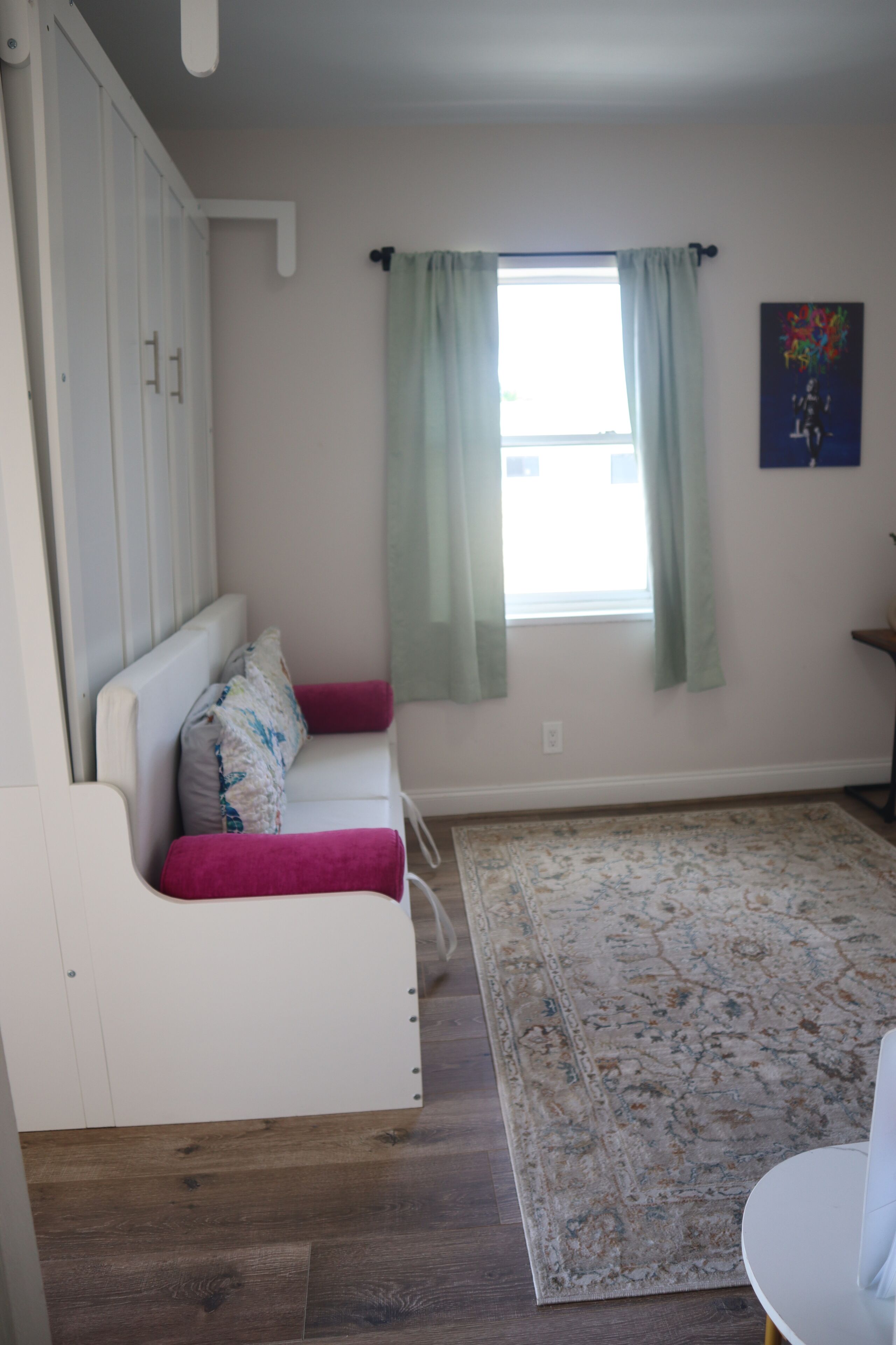 Une pièce avec un canapé blanc, un tapis à motifs, une fenêtre avec des rideaux verts et une petite table.